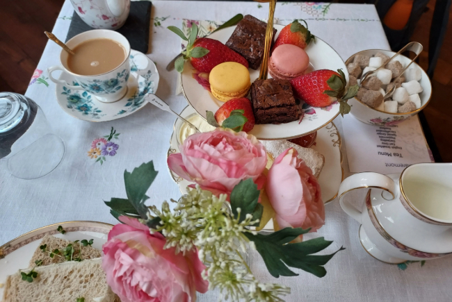 Table full of afternoon tea treats, tea, sandwiches and cakes. 